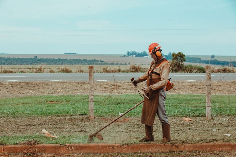 Jardineiro do Grupo Distrital com equipamentos de proteção realizando roçagem de área verde