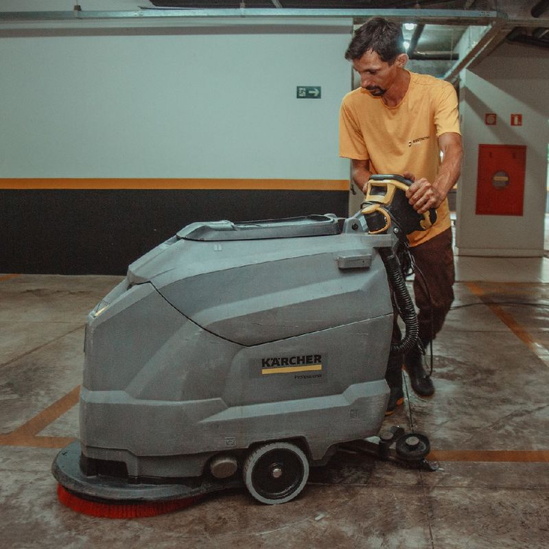 Operador com lavadora industrial de piso em garagem de edifício